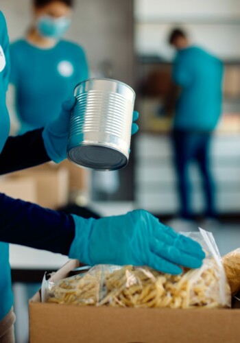 Unrecognizable female volunteer packing food in donation box while working at charity foundation.
